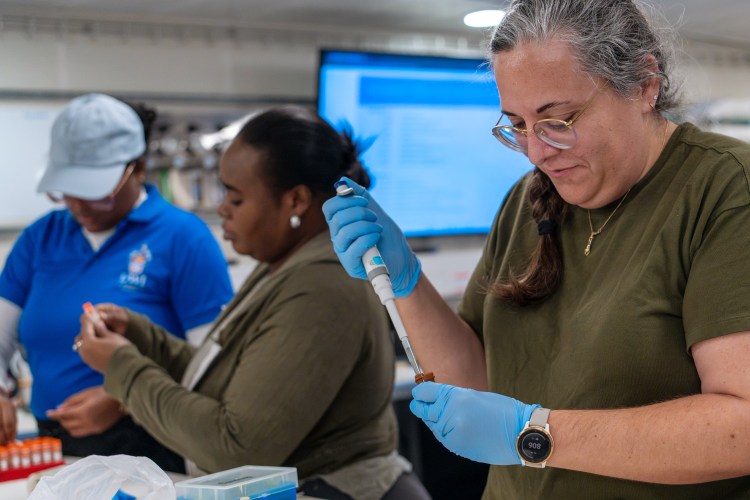 Three individuals in a laboratory setting are engaged in precise scientific tasks, with one person carefully handling a pipette.